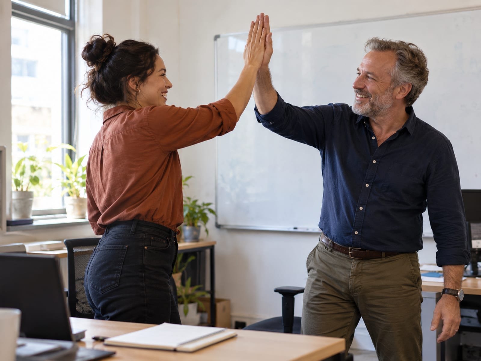 Two coworkers giving each other a quick high five beside a whiteboard