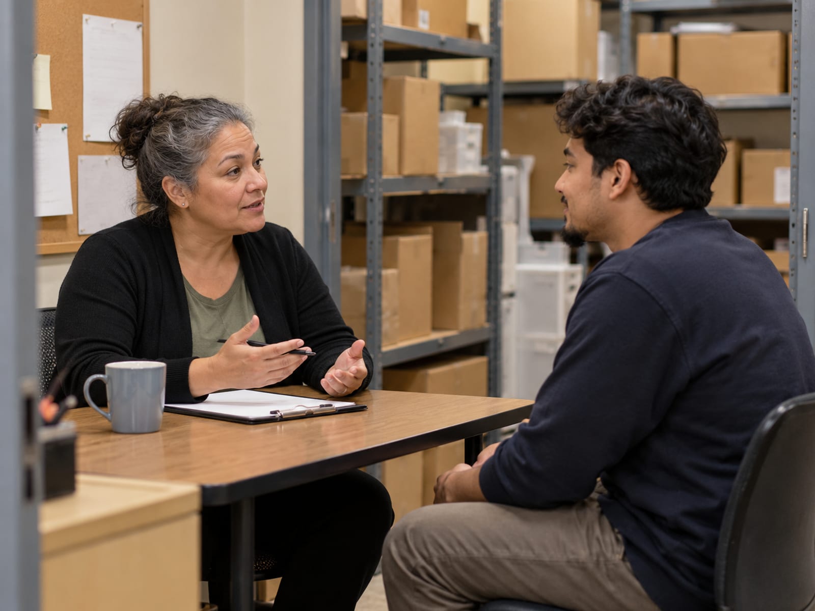 A supervisor and an employee talking during a review in a stockroom office